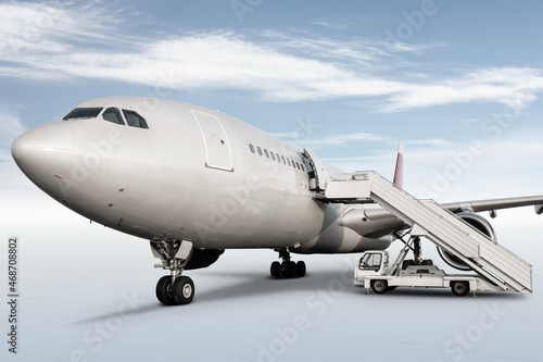 Wide body passenger aircraft with air-stairs at the airport apron isolated on bright background with sky