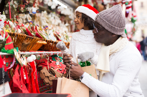 Man and smiling girl with toy in hand choosing decorations at Christmas market