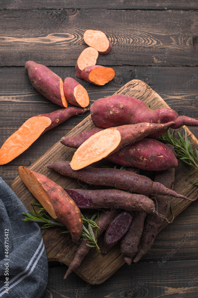 Sweet potato on wooden board background, close up. Raw sweet potatoes or batatas with herbs Sweet potato on wooden board background, close up. Raw sweet potatoes or batatas with herbs