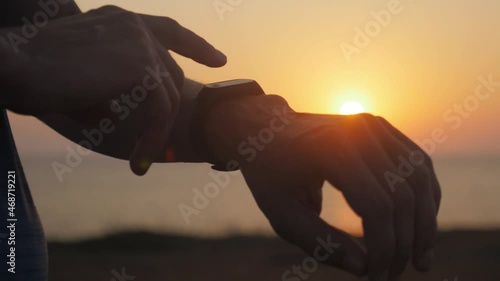 closeup of male hand arm with smart watch checking time results of outdoor sport training activity in summer sunset
