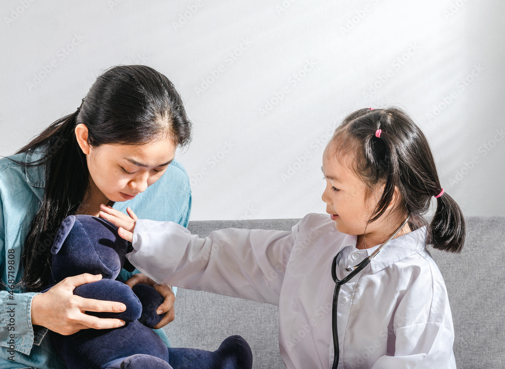 Girl with stethoscope playing doctor or nurse and patient game checking fever bear toy having fun at a home sofa with mother, cute small child play takes care of a bear friend, home family activity Girl with stethoscope playing doctor or nurse and patient game checking fever bear toy having fun at a home sofa with mother, cute small child play takes care of a bear friend, home family activity