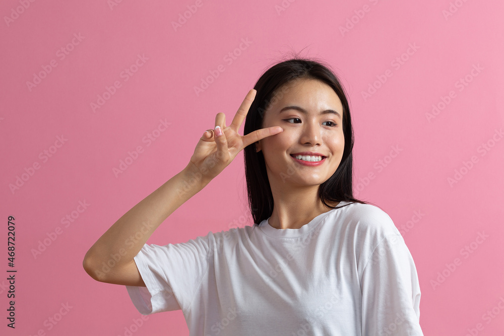 Portrait of asian positive smiling young woman with V fingers gesture on pink background. Portrait of asian positive smiling young woman with V fingers gesture on pink background.