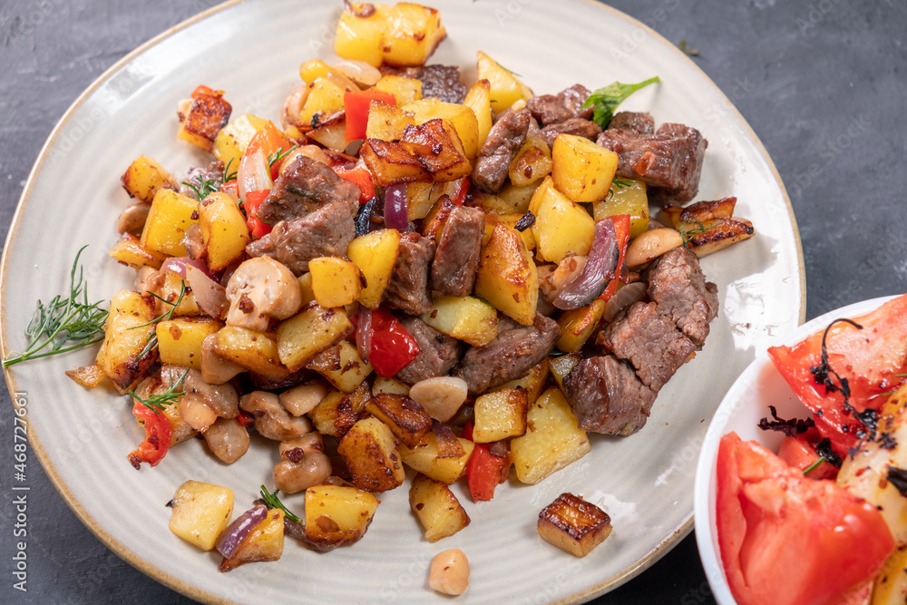 Fried potatoes with mushrooms and meat in a round plate close-up. Fried potatoes with mushrooms and meat in a round plate close-up.