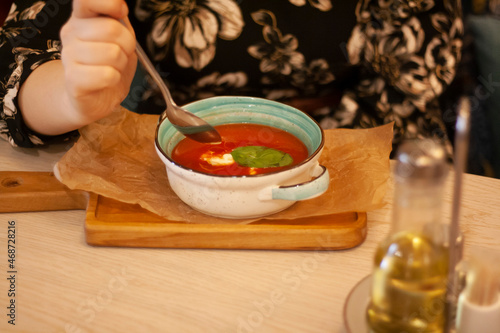 A woman is eating tomato soup with a spoon