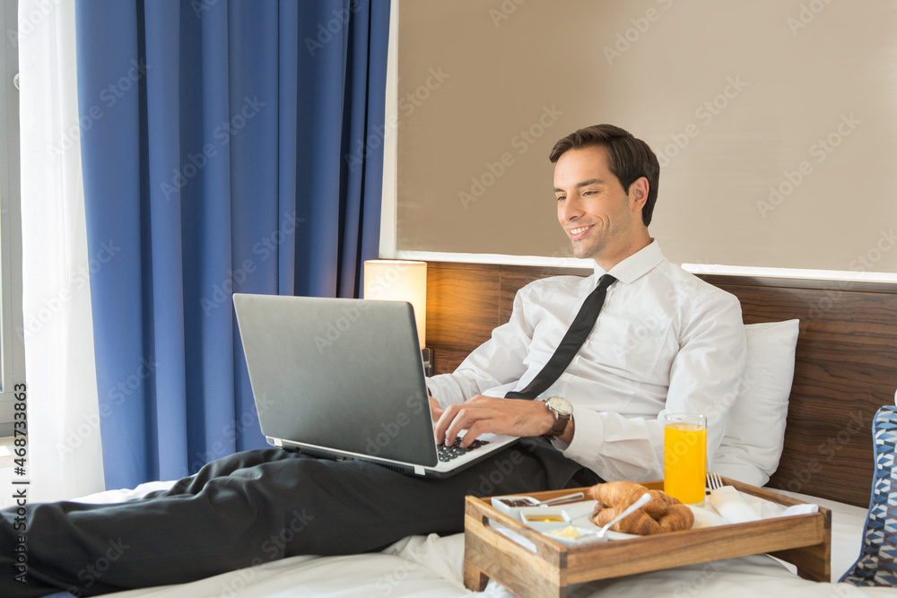 Happy businessman in suit working on the hotel bed on his computer laptop notebook Happy businessman in suit working on the hotel bed on his computer laptop notebook