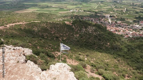 Aerial view of torn Greek flag and countryside over the top of a mountain