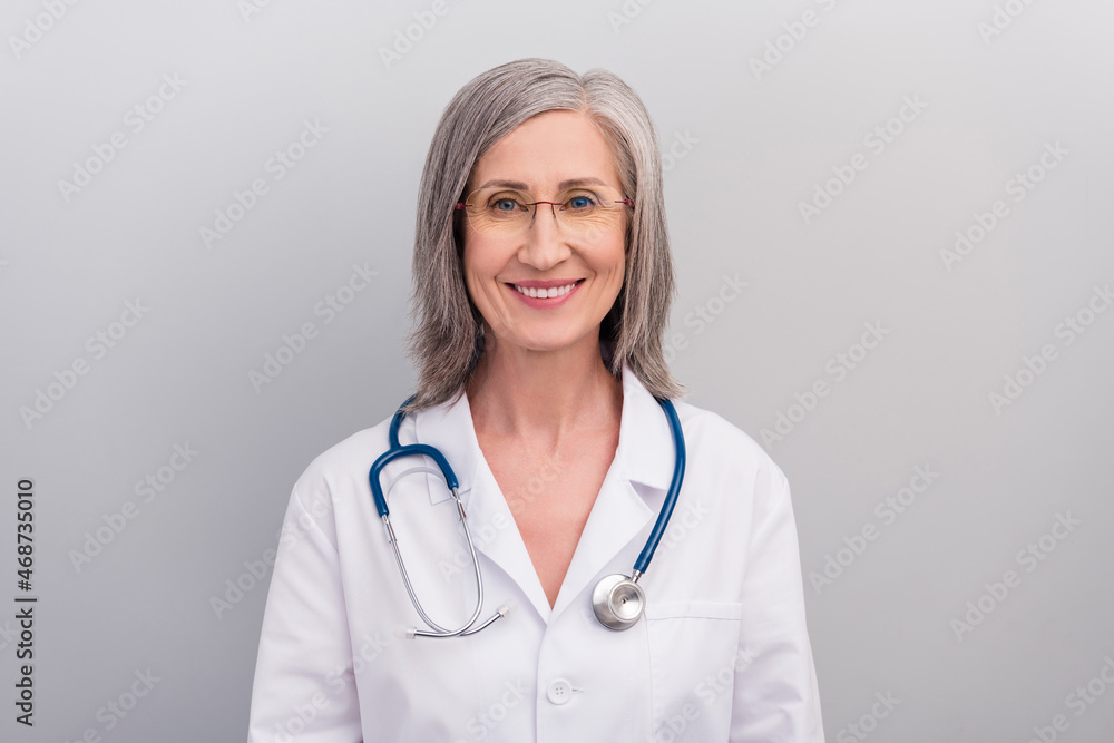 Photo of cheerful positive mature lady doctor wear white coat spectacles smiling isolated grey color background
