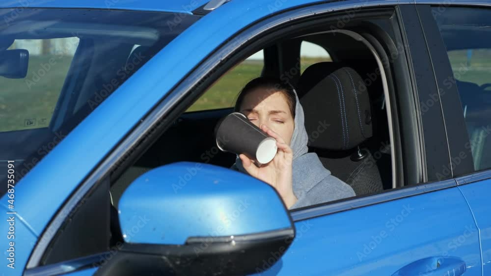 Woman wrapped in warm scarf with brunette hair finishes drinking hot coffee and throws plastic cup away out of car window on autumn street closeup Woman wrapped in warm scarf with brunette hair finishes drinking hot coffee and throws plastic cup away out of car window on autumn street closeup