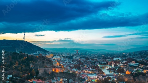 Tbilisi  Georgia. Top View Of Famous Landmarks In Night Illuminations. Georgian Capital Skyline Cityscape. City During Sunset And Night Illuminations. Day To Night Transition