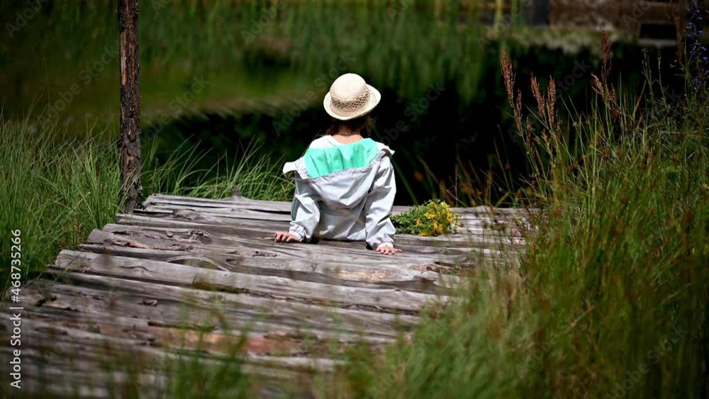 Video with a rear view of a girl with a hat, walking and sitting on a wooden pier of a mountain lake holding a bouquet of herbs