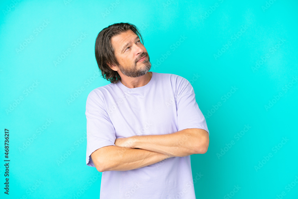 Senior dutch man isolated on blue background looking up while smiling Senior dutch man isolated on blue background looking up while smiling