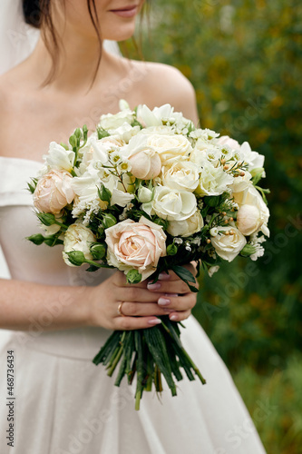 The bride in a wedding dress with open shoulders holds a bouquet of roses