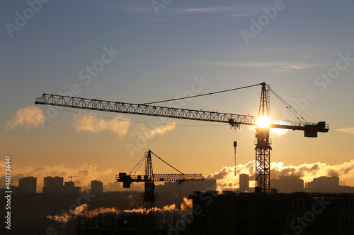Silhouettes of construction cranes and unfinished residential buildings on sunrise background. Housing construction, apartment block in city