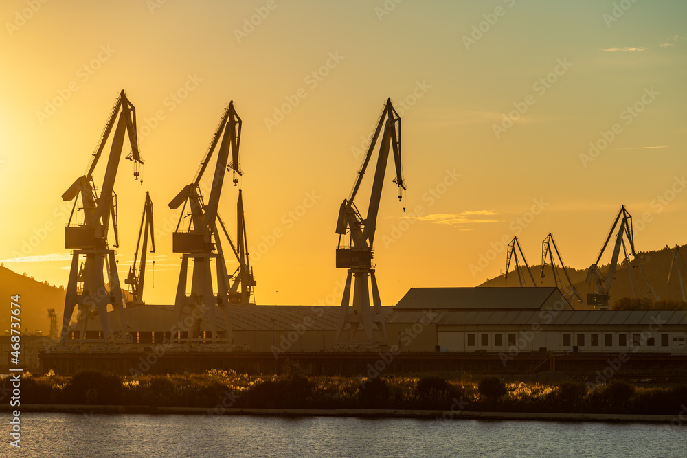 Group of shipyard cranes against yellow sky at sunset in Ferrol, Galicia, Spain
