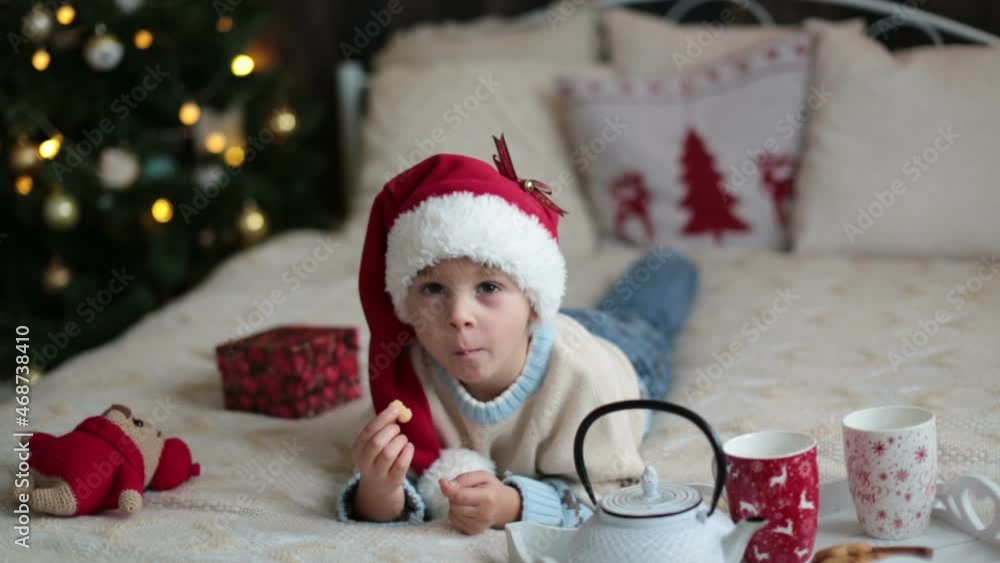 Cute toddler child, boy in a Christmas outfit, playing in a wooden cabin on Christmas, decoration around him. Child reading book and drinking tea Cute toddler child, boy in a Christmas outfit, playing in a wooden cabin on Christmas, decoration around him. Child reading book and drinking tea