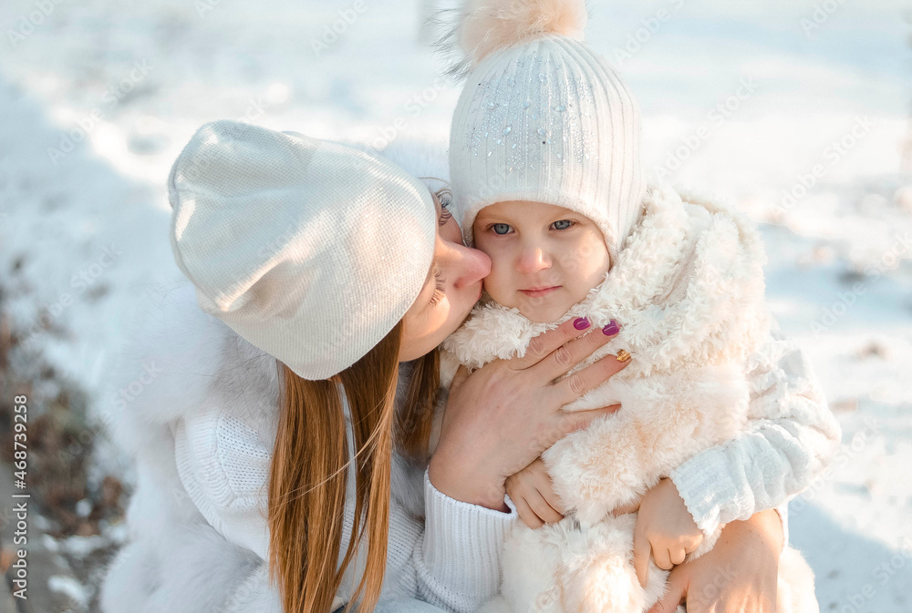 Happy family walks on snowy day. Little girl with her mother in winter park. A young and happy mother holds a child in her arms, smiles and rejoices. Street of winter fresh air, concept of recreation Happy family walks on snowy day. Little girl with her mother in winter park. A young and happy mother holds a child in her arms, smiles and rejoices. Street of winter fresh air, concept of recreation
