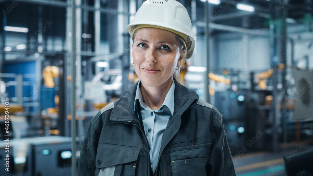 Car Factory Office: Portrait of Female Chief Engineer Wearing Hard Hat Looking at Camera, Smiling. Professional Technician. Automated Robot Arm Assembly Line Manufacturing High-Tech Electric Vehicles Car Factory Office: Portrait of Female Chief Engineer Wearing Hard Hat Looking at Camera, Smiling. Professional Technician. Automated Robot Arm Assembly Line Manufacturing High-Tech Electric Vehicles