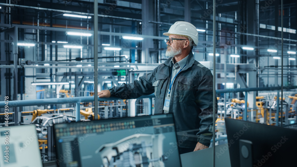 Car Factory: Confident Male Automotive Engineer Wearing Hard Hat, Standing and Monitoring Equipment Production Line. Automated Robot Arm Assembly Line Manufacturing Electric Vehicles Car Factory: Confident Male Automotive Engineer Wearing Hard Hat, Standing and Monitoring Equipment Production Line. Automated Robot Arm Assembly Line Manufacturing Electric Vehicles