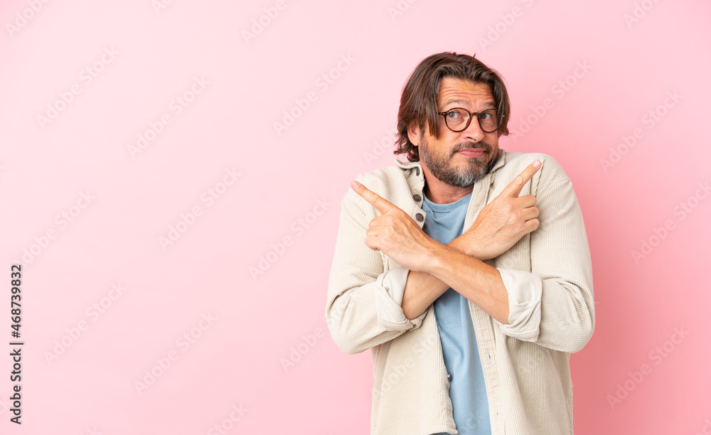 Senior dutch man isolated on pink background pointing to the laterals having doubts Senior dutch man isolated on pink background pointing to the laterals having doubts