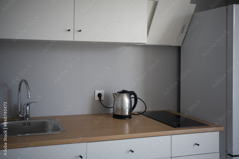 modern kitchen interior. white facades, gray walls. steel-colored teapot on a wooden tabletop. modern kitchen interior. white facades, gray walls. steel-colored teapot on a wooden tabletop.