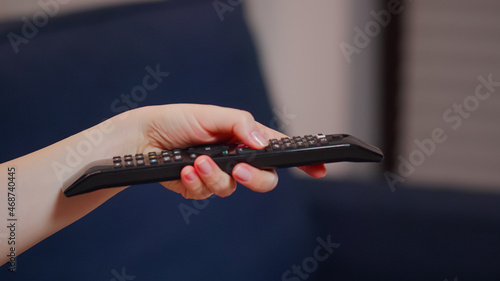 Close up of caucasian hand with TV remote switching channels while sitting on couch. Young person using technology finding movie to watch and relax after dinner  laying on sofa.