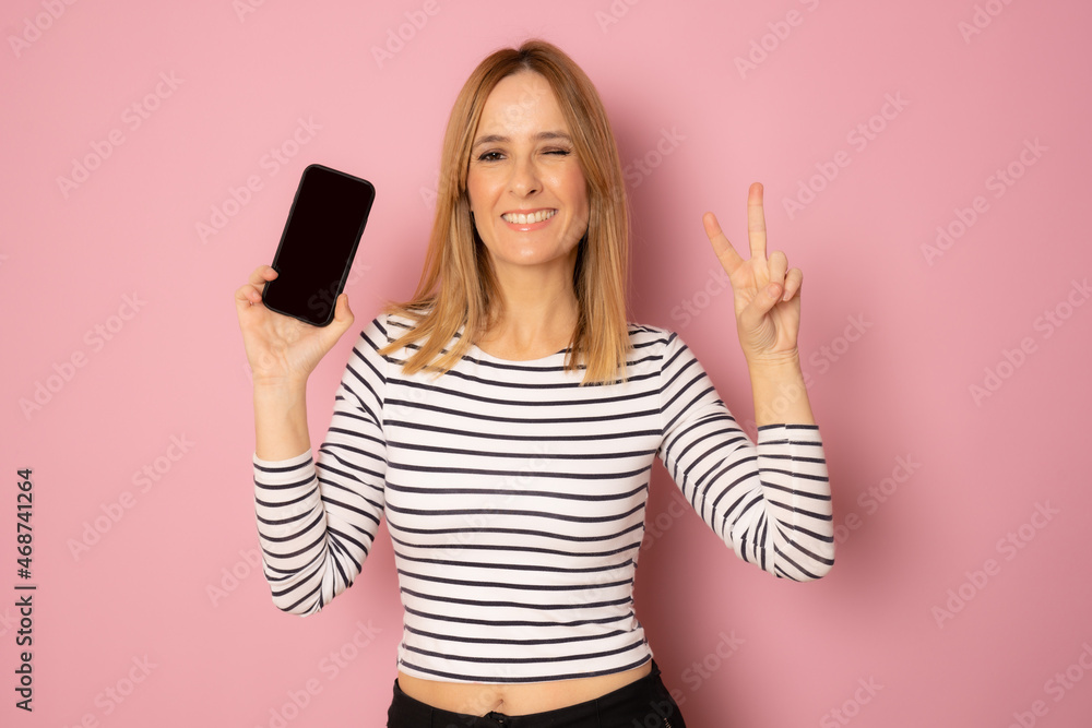 Happy woman holding mobile phone with victory sign isolated over pink background. Happy woman holding mobile phone with victory sign isolated over pink background.