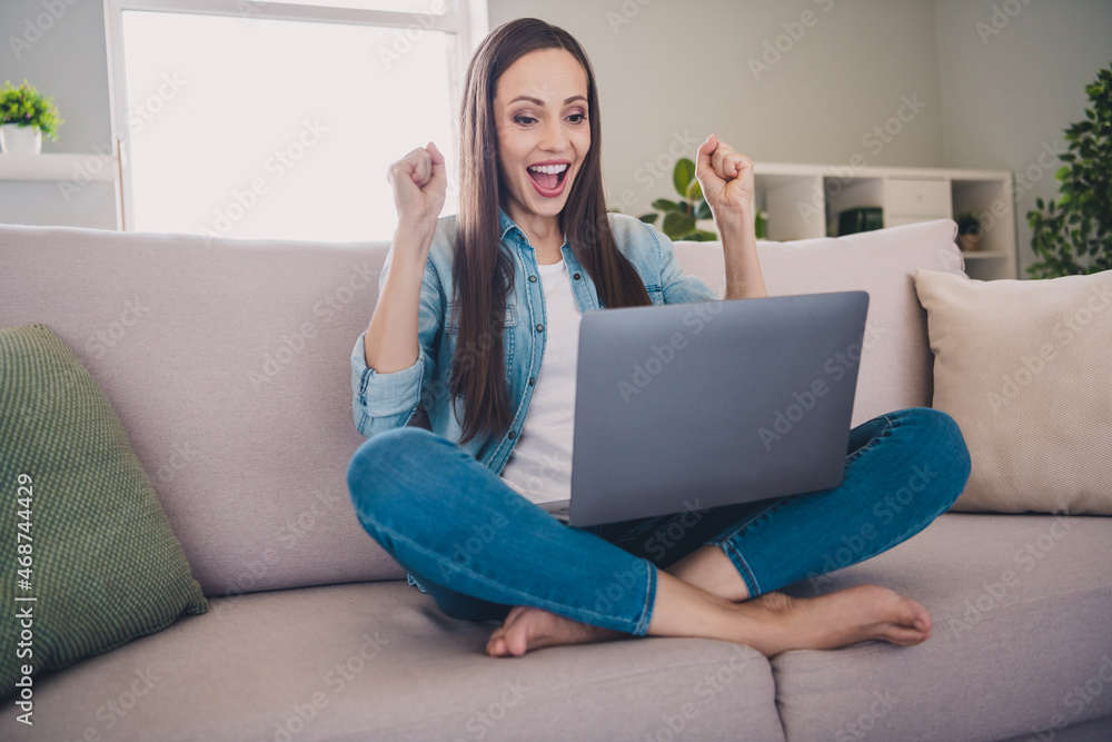 Portrait of attractive cheerful lucky long-haired woman sitting on divan using laptop rejoicing having fun at home indoors Portrait of attractive cheerful lucky long-haired woman sitting on divan using laptop rejoicing having fun at home indoors