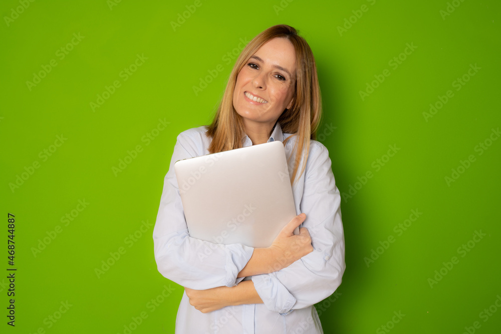 Portrait of young businesswoman holding silver laptop in the office isolated over green background