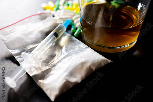 Hard drugs and alcohol on dark gray table. Alcohol pills syringe plastic bag powder of cocaine on table with shadow.Closeup.Copy space. photo