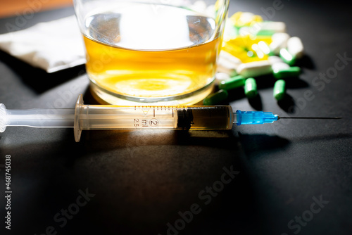 Hard drugs and alcohol on dark gray table. Alcohol pills syringe plastic bag powder of cocaine on table with shadow.Closeup.Copy space. photo