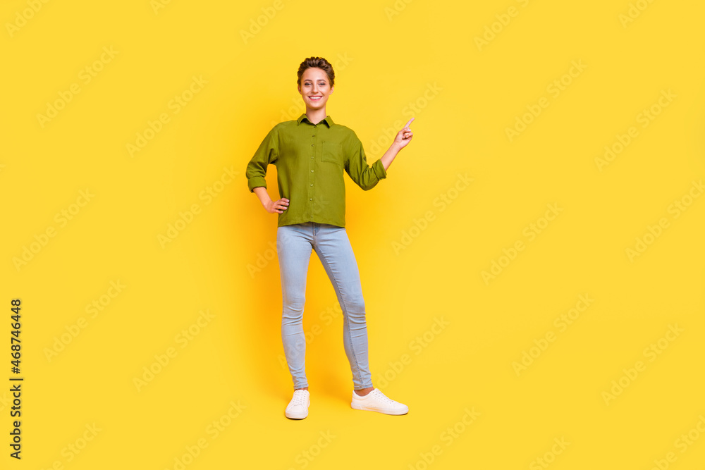 Photo of promoter lady arm hip direct finger empty space wear green shirt jeans shoes isolated yellow color background Photo of promoter lady arm hip direct finger empty space wear green shirt jeans shoes isolated yellow color background