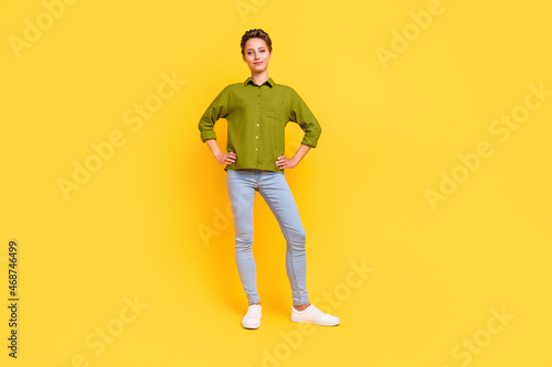 Photo of confident successful lady hands hips posing wear green shirt jeans footwear isolated yellow color background