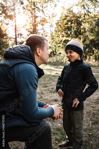 Boy and dad are playing on a walk in the park. The boy makes a joke. Walking son and dad in the autumn sunny park.