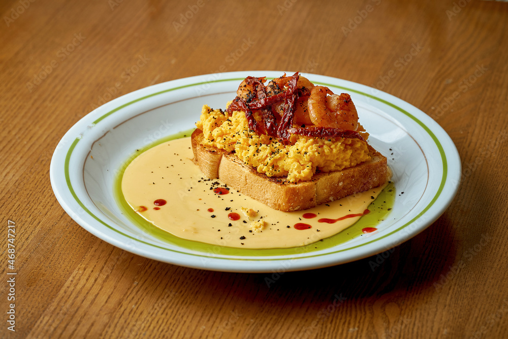Toast with scrambled eggs and shrimps in a white plate Toast with scrambled eggs and shrimps in a white plate
