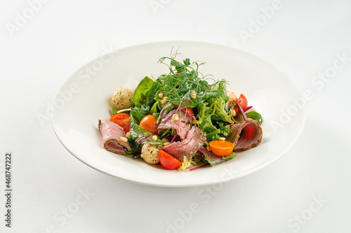 Salad with roast beef and pine nuts in a white plate.