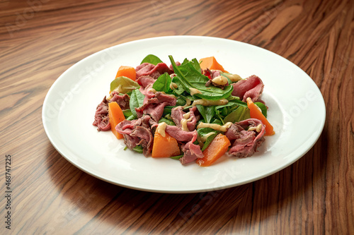 Salad with roast beef and pumpkin in a white plate.