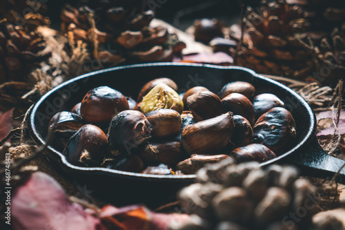 Roasted chestnuts in a small iron pan on a table with autumn leaves and pine cones. Ready to eat. Traditional autumn food.