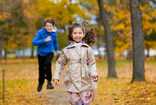 Children run along path in autumn park. They play and laugh, they have a lot of fun. Beautiful nature and trees with yellow leaves.