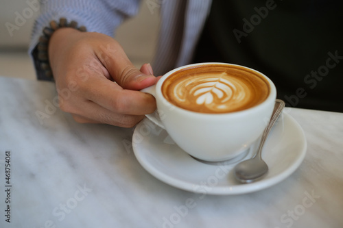 Closeup image of a young smart man holding a coffee cup with latte art in the comfortable living room.