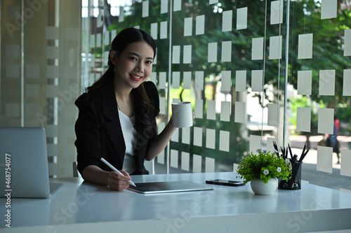 Photo of a young designer holding a coffee cup while using a digital tablet and stylus pen at the smart working desk over the modern office as a background. photo