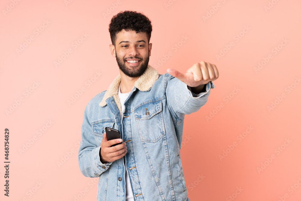 Young Moroccan man using mobile phone isolated on pink background giving a thumbs up gesture Young Moroccan man using mobile phone isolated on pink background giving a thumbs up gesture