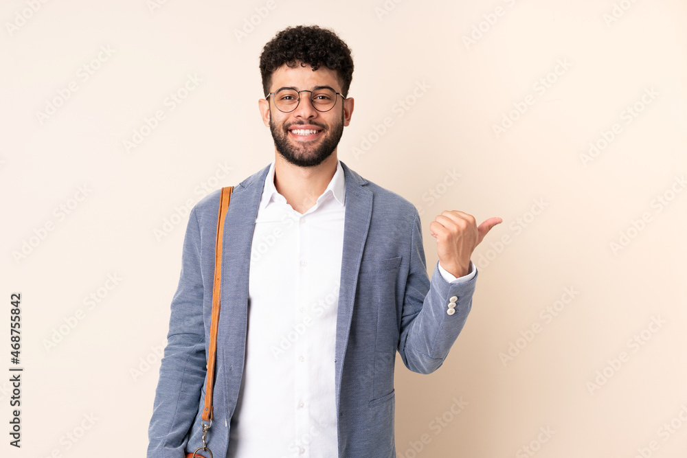 Young business Moroccan man isolated on beige background pointing to the side to present a product Young business Moroccan man isolated on beige background pointing to the side to present a product