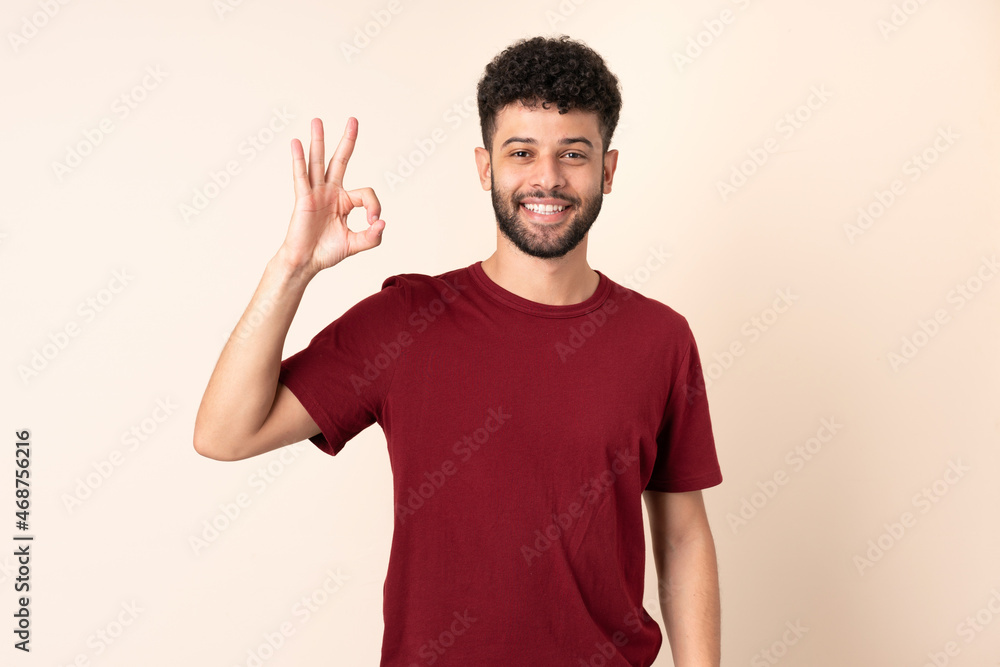 Young Moroccan man isolated on beige background showing ok sign with fingers Young Moroccan man isolated on beige background showing ok sign with fingers
