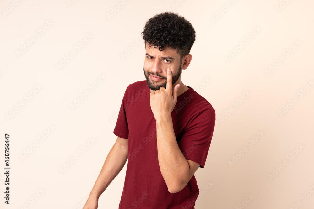 Young Moroccan man isolated on beige background showing something Young Moroccan man isolated on beige background showing something