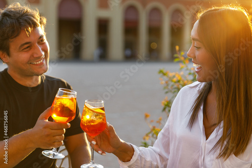 Young couple smiling and toasting with aperol spritz at sunset