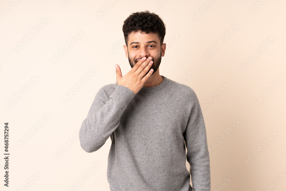 Young Moroccan man isolated on beige background happy and smiling covering mouth with hand Young Moroccan man isolated on beige background happy and smiling covering mouth with hand