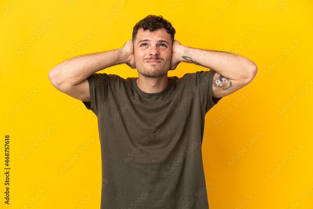 Young caucasian handsome man isolated on yellow background frustrated and covering ears Young caucasian handsome man isolated on yellow background frustrated and covering ears