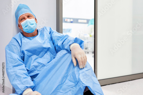 Arzt in Schutzkleidung sitzt ausgebrannt und m  de am Boden