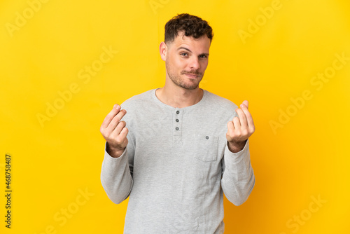 Young caucasian handsome man isolated on yellow background making money gesture