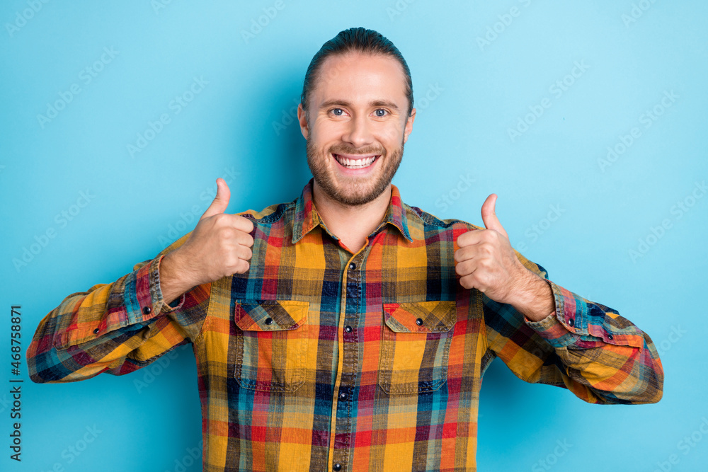 Photo of cool young brunette guy show thumb up wear yellow shirt isolated on blue color background Photo of cool young brunette guy show thumb up wear yellow shirt isolated on blue color background